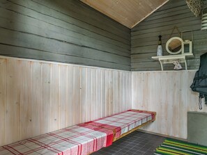 A sauna room with a bench, a shelf with a bottle and a mirror, and a striped rug.