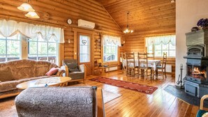 A log cabin interior with a dining area, fireplace, and large windows.