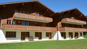 A multi-story wooden building with balconies, large windows, and a well-maintained lawn.