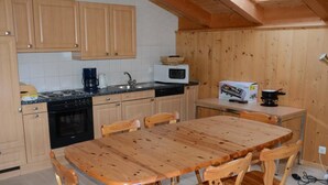 A compact kitchen with wooden cabinets, a stove, a microwave, and a dining table with wooden chairs.
