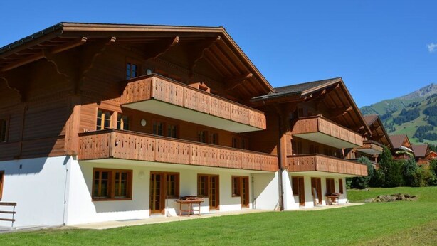 A large wooden chalet with multiple balconies, a covered porch, and a mountain backdrop.