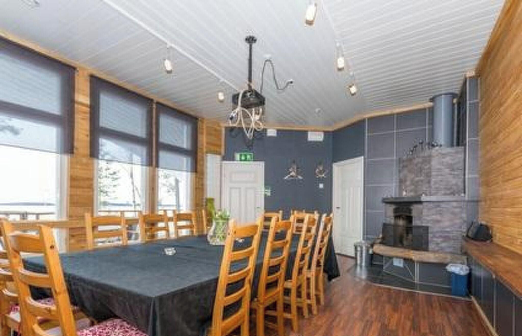 Comedor con sillas de madera y una mesa, zona de cocina con estufa, y vistas al exterior a través de amplios ventanales.