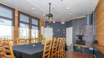 Comedor con sillas de madera y una mesa, zona de cocina con estufa, y vistas al exterior a través de amplios ventanales.