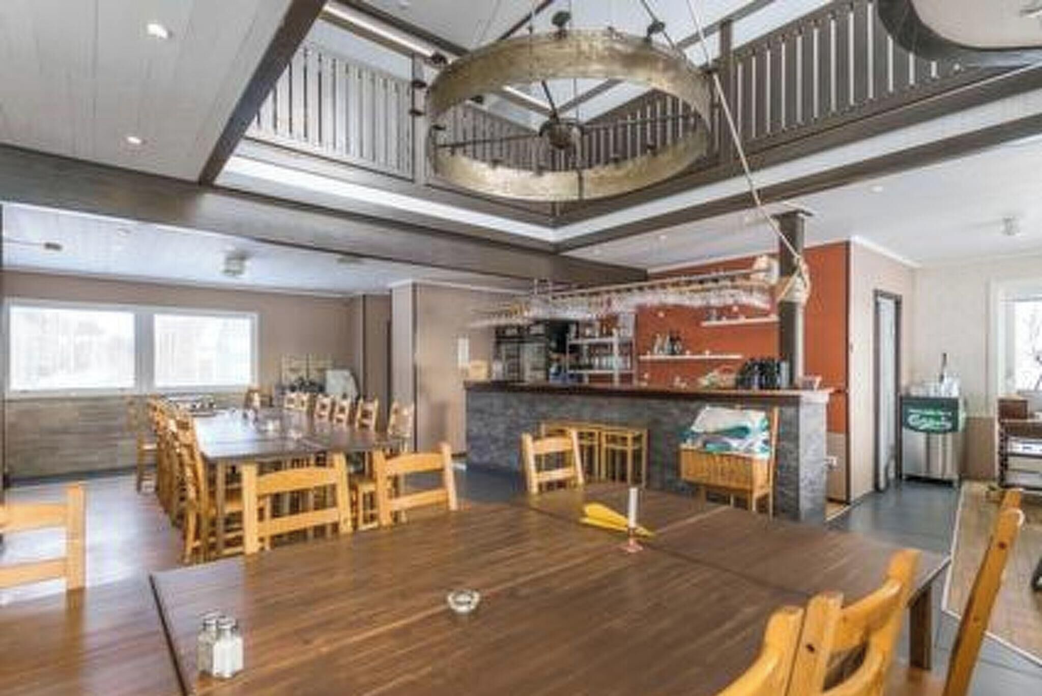 A spacious dining area with a large wooden table and chairs, a kitchen area with a bar, and a staircase leading to an upper level.