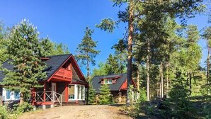 A cabin with a red roof and white walls, surrounded by tall pine trees. - Hästöskata b by Interhome (Kruunupyy)
