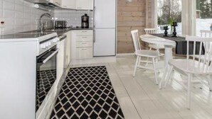 A modern kitchen with white cabinets, a microwave, and a refrigerator. There is a dining area with white chairs and a table. - Hästöskata b by Interhome (Kruunupyy)