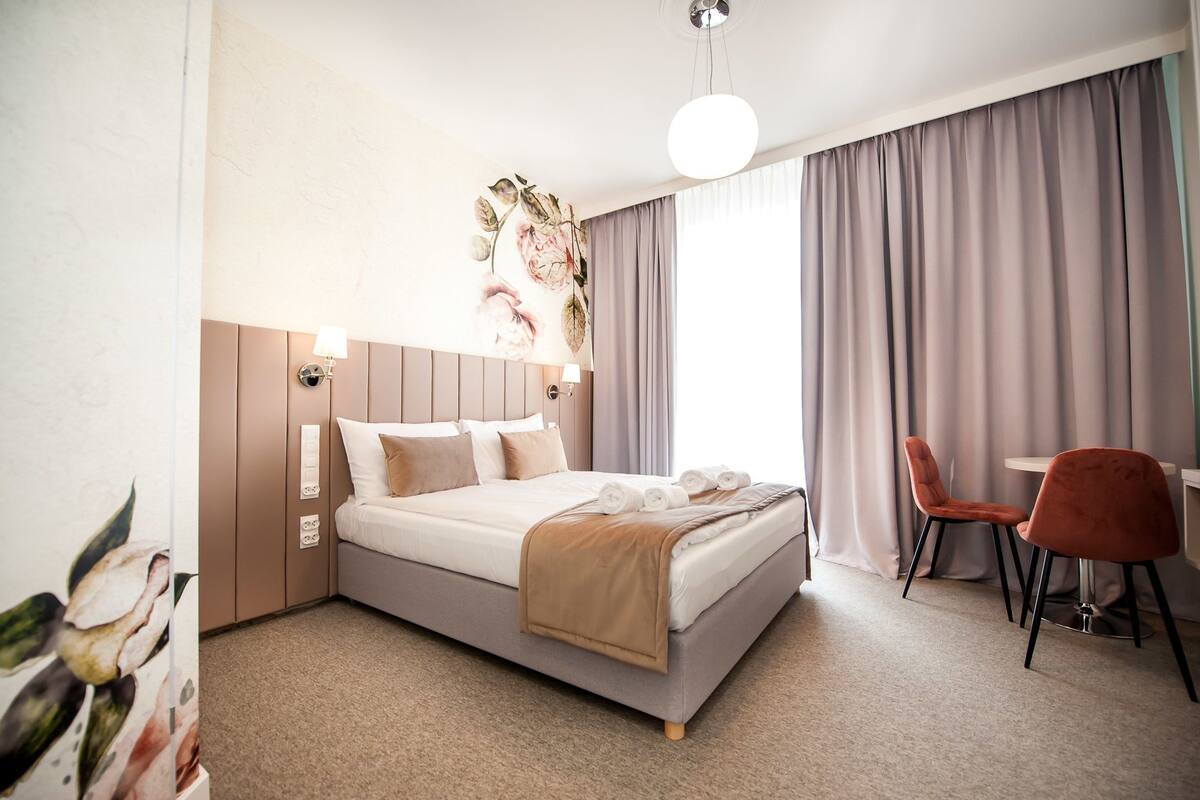 A modern hotel room with a large bed, a desk with two chairs, and a view of the outdoors.