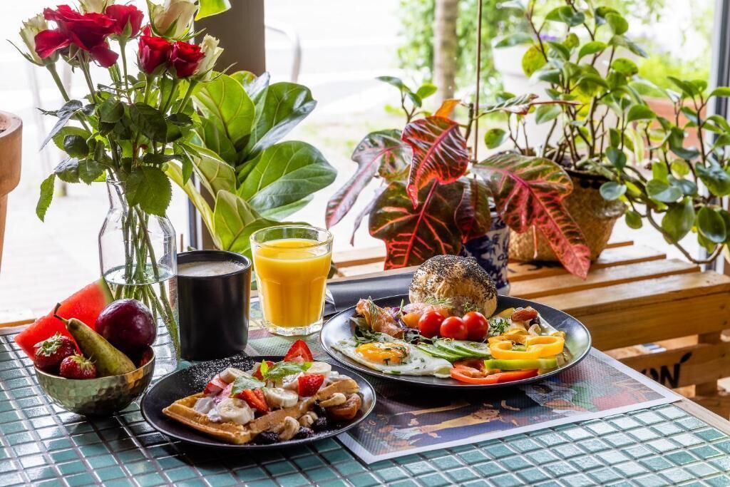 Ett frukostbord med ett urval av rätter, ett glas apelsinjuice och en vas med röda rosor.