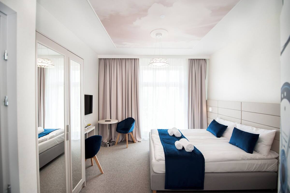 A modern hotel room with a bed, a desk, a chair, and a TV.