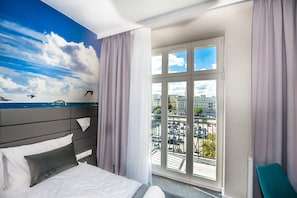 A hotel room with a bed, a view of the city through large windows, and a mural of the sky and sea on the wall. - Hotel Gdynia Boutique (Gdynia)