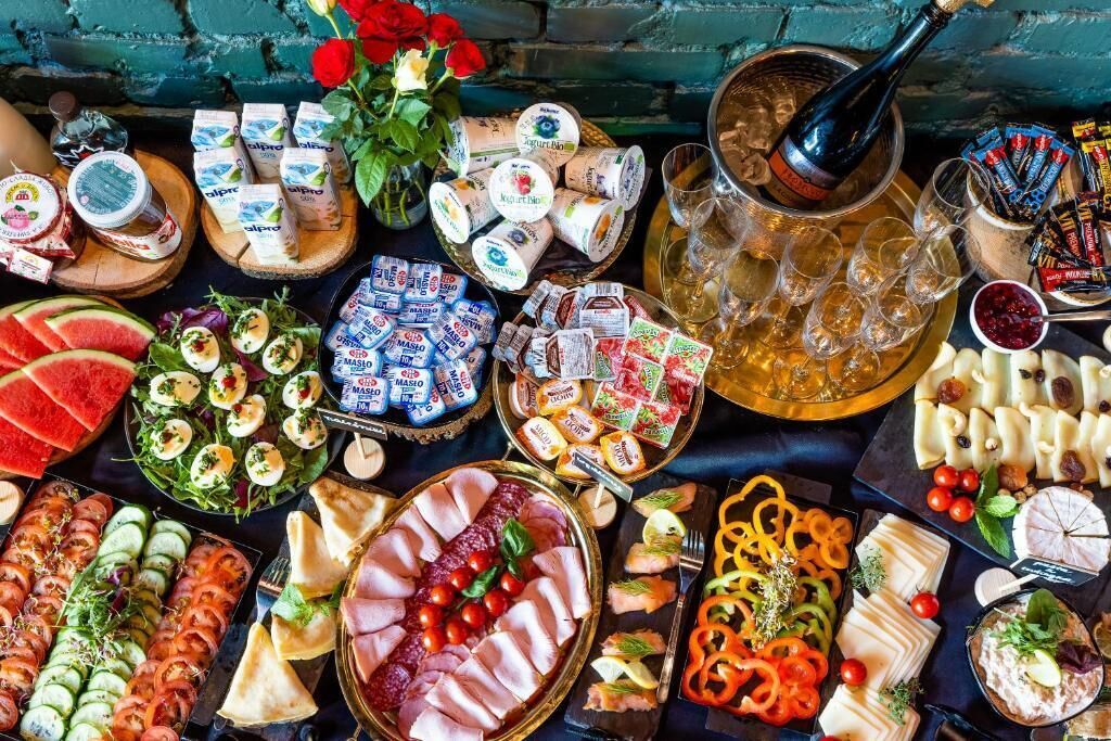 Diversa selección de alimentos y bebidas, como quesos, embutidos y aperitivos, dispuesta sobre una mesa.