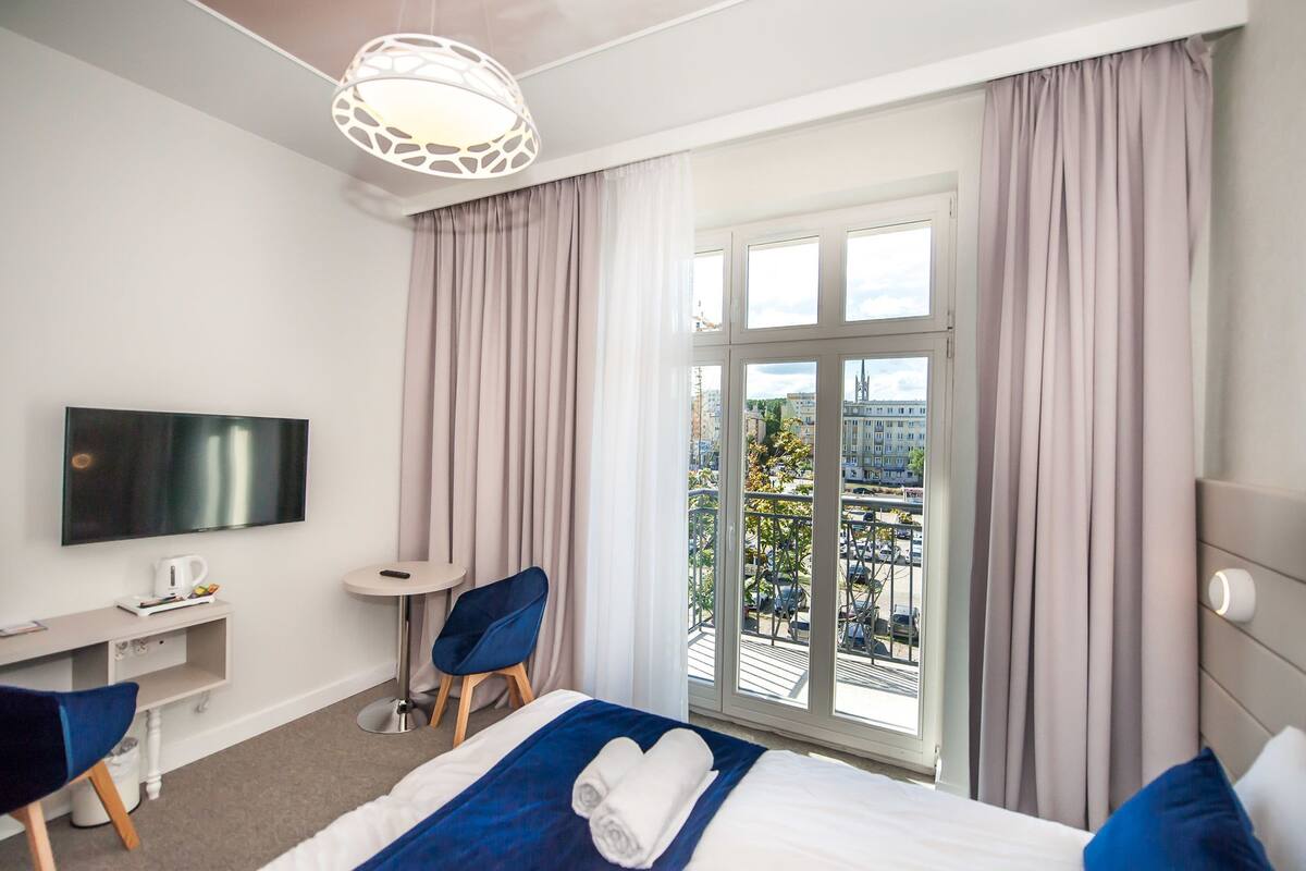 A hotel room with a bed, a desk, a chair, a television, and a window with a city view.