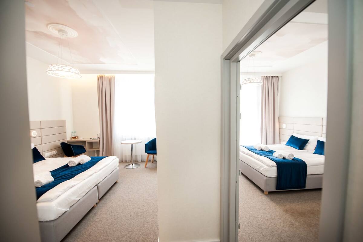 A hotel room with two beds, a small table, and a mirror.