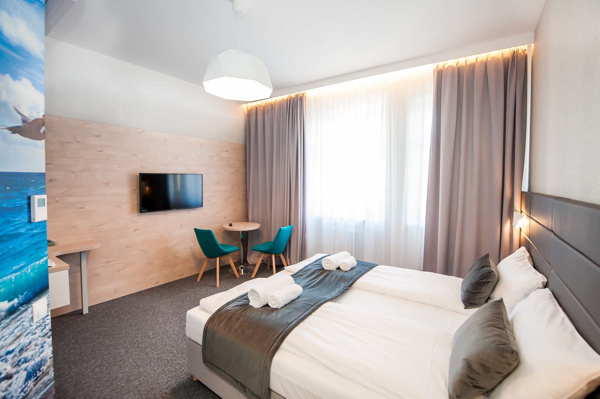 Ett hotellrum med en säng, ett skrivbord med en stol, en TV och ett fönster med gardiner.