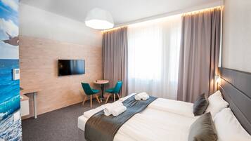 Ett hotellrum med en säng, ett skrivbord med en stol, en TV och ett fönster med gardiner.