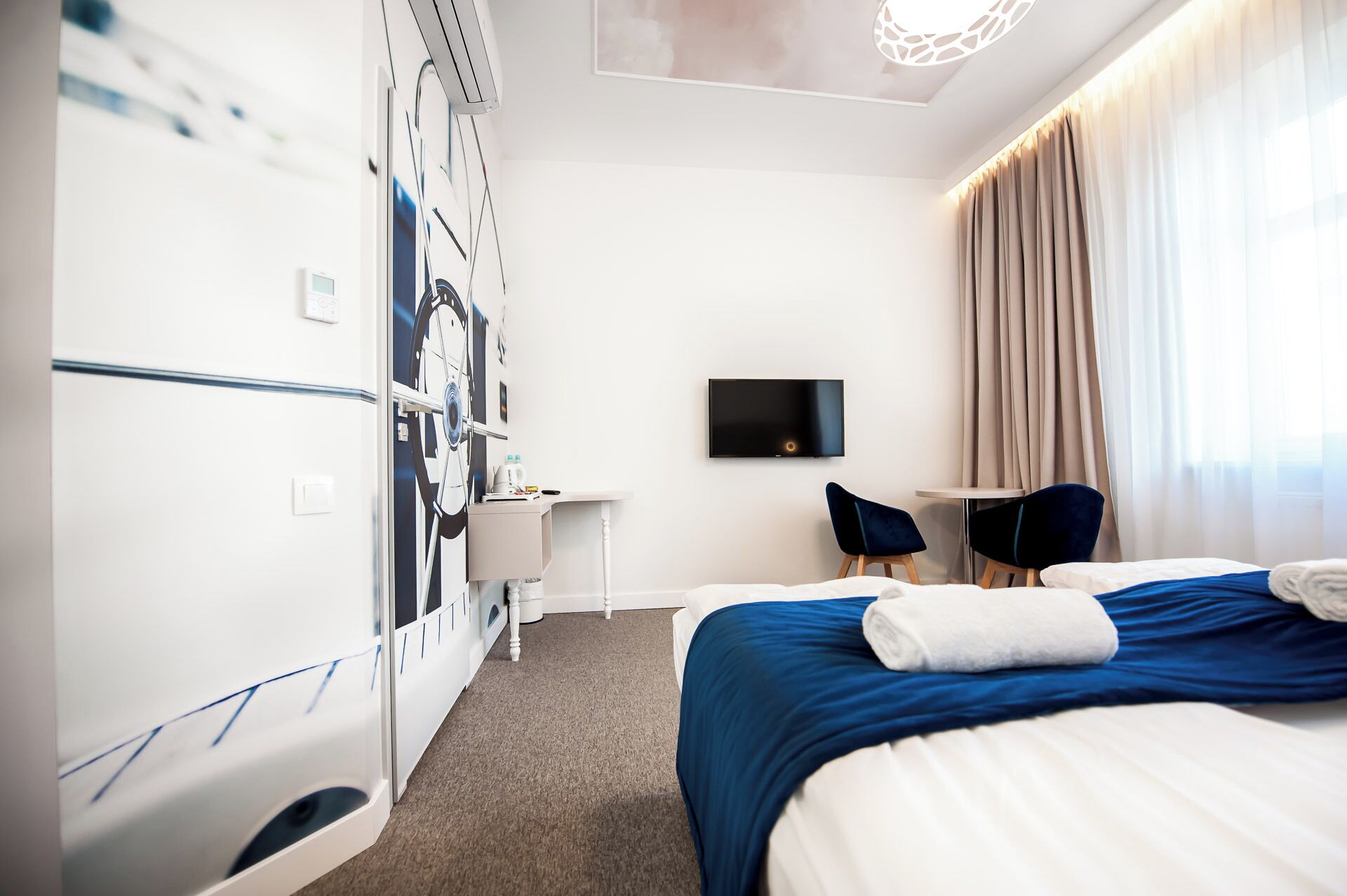 A hotel room with a bed, a desk, a chair, a TV, and a wall-mounted air conditioning unit.