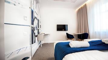 A hotel room with a bed, a desk, a chair, a TV, and a wall-mounted air conditioning unit.