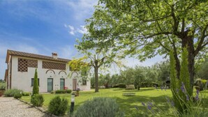 A two-story house with a tiled roof, a stone facade, and a well-maintained garden with a lawn, trees, and shrubs. - Oliveto by Interhome (Vinci)