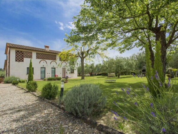 Una casa de dos pisos con techo de tejas, fachada de piedra y un jardín bien cuidado con césped, árboles y arbustos.