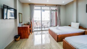 Habitación de hotel con cama, escritorio con espejo, televisión y balcón con vista a edificios.