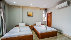 Habitación de hotel con dos camas de madera, un cuadro en la pared, un equipo de aire acondicionado y una puerta de madera.