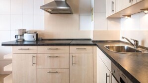 Una cucina moderna con mobili chiari in legno, un lavello in acciaio inox e una cappa aspirante.
