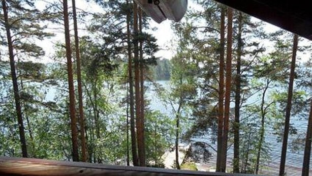 A view from a wooden deck overlooking a lake surrounded by tall trees.