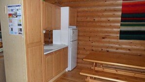 A compact kitchen with wooden cabinets, a white refrigerator, and a wooden bench.