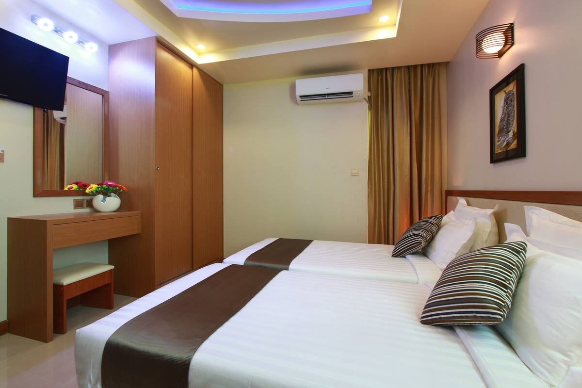 A hotel room with a bed, a desk, a chair, a TV, an air conditioner, and a painting on the wall.