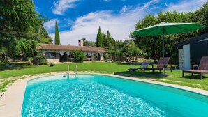 A swimming pool with clear blue water, surrounded by a well-maintained lawn and trees. There are lounge chairs and a green umbrella providing shade. - Vacation home Moira by Interhome (Umag)