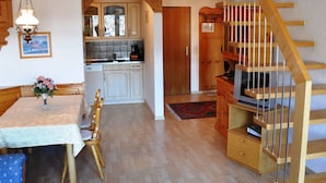 A kitchen with wooden cabinets, a dining table with chairs, a wooden staircase, and a chandelier. - Disentiserhof Hönig by Interhome (Disentis)
