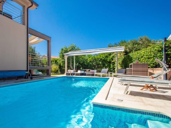 A swimming pool with lounge chairs and a pergola, surrounded by greenery.