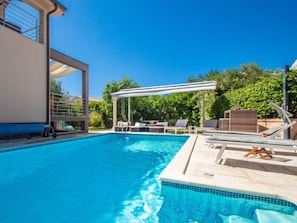 Piscina con sillas de descanso y una pérgola, rodeada de vegetación.