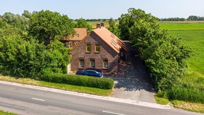 A two-story brick house with a sloped roof, a car parked in front, and a road beside it. - Apartment Krause by Interhome (Norden)