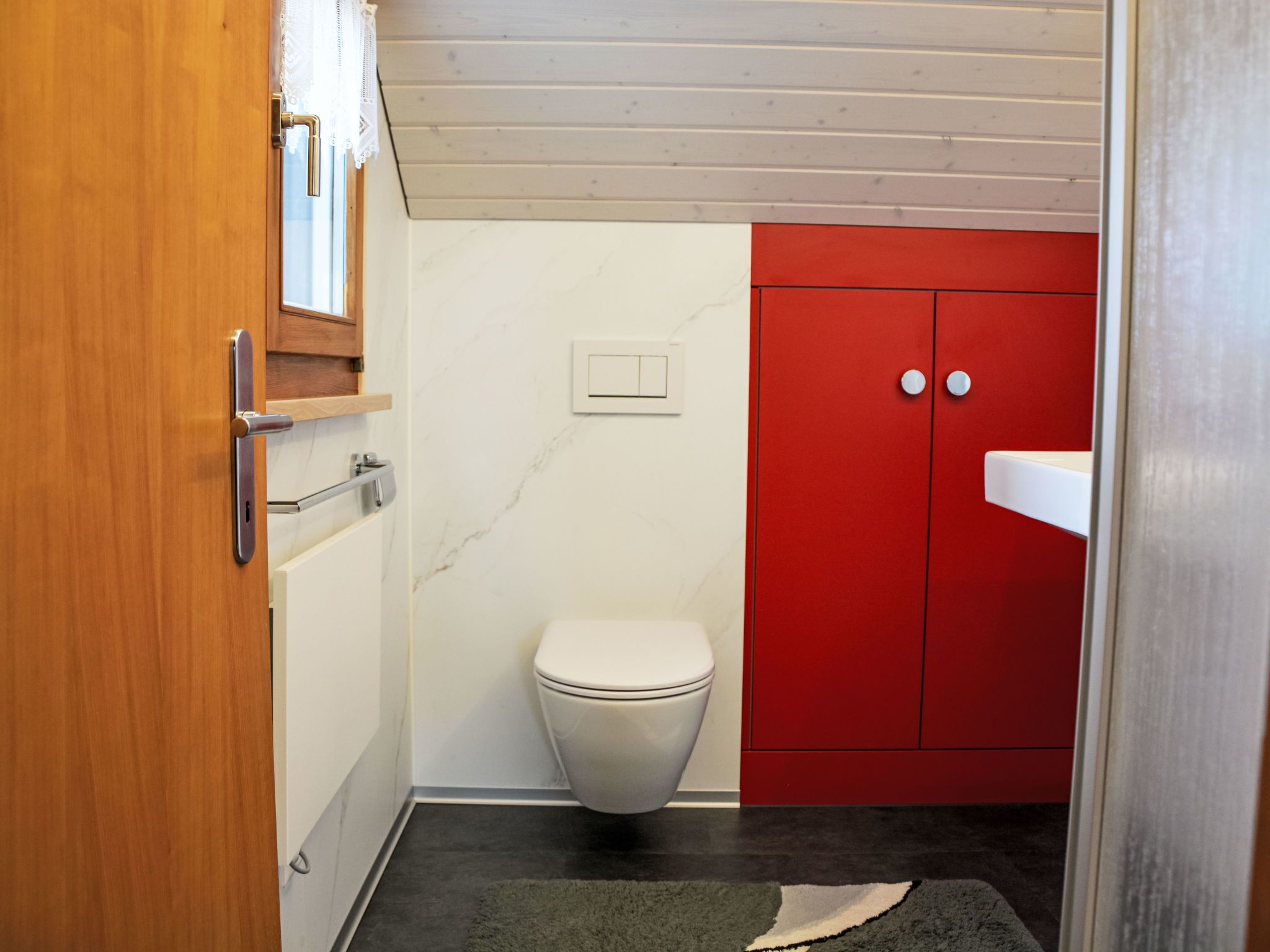 A small bathroom with a toilet, a red cabinet, and a white sink.
