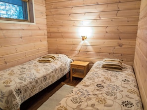 A small, cozy room with two single beds, a nightstand, and a wall-mounted light fixture.