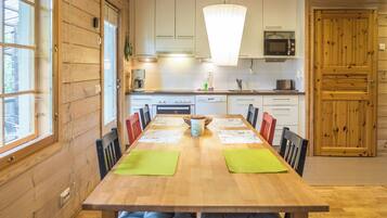 Un interior de madera con una larga mesa de comedor, sillas, una zona de cocina con microondas y un reloj en la pared.