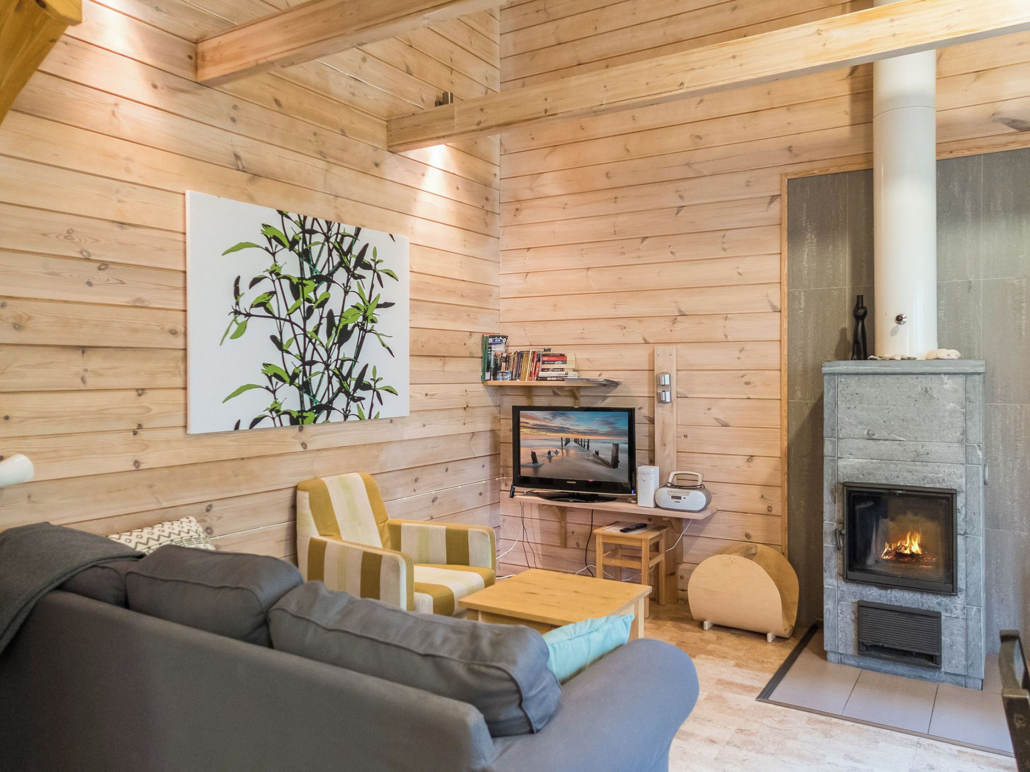 A cozy living room with a sofa, armchair, TV, fireplace, and a wall-mounted bookshelf.