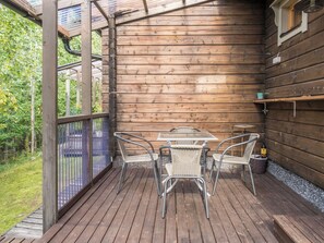 Een houten terras met een glazen tafel en stoelen, omgeven door een houten chalet.
