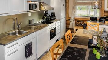 Une cuisine moderne équipée d’appareils électroménagers en acier inoxydable, un coin repas avec une table dressée pour quatre personnes et une fenêtre donnant sur l’extérieur.