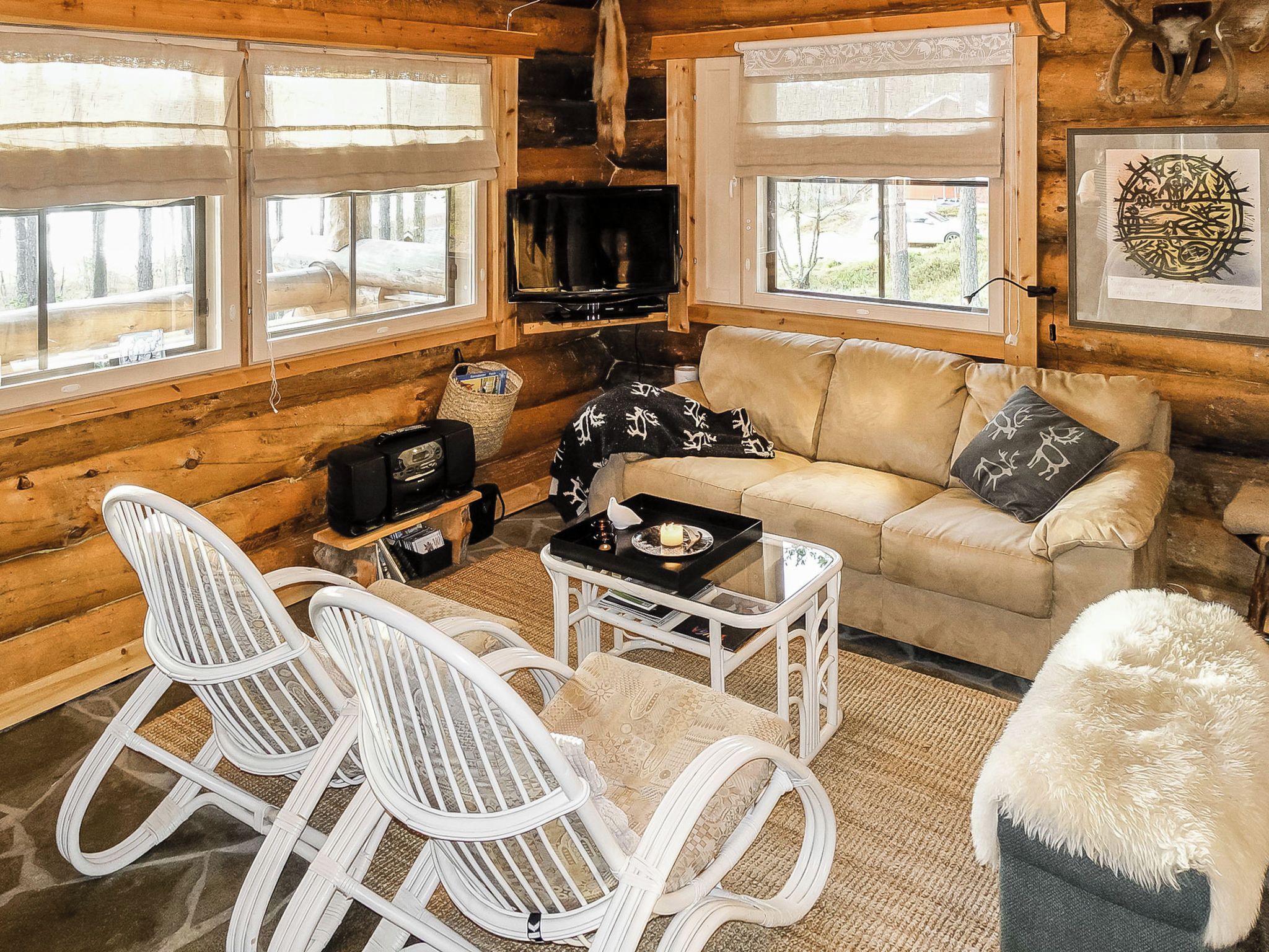 A cozy log cabin interior with a sofa, two rocking chairs, a television, and a fireplace.