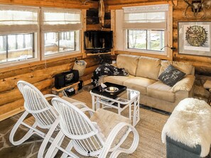 Interior acogedor de una cabaña de madera con un sofá, dos mecedoras, un televisor y una chimenea.