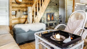 L’intérieur d’un chalet confortable, avec une cheminée en pierre, un escalier en bois et une chaise blanche agrémentée d’un coussin à motifs.