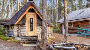 Une cabane en rondins avec une porte en bois et une cheminée, entourée d’arbres.