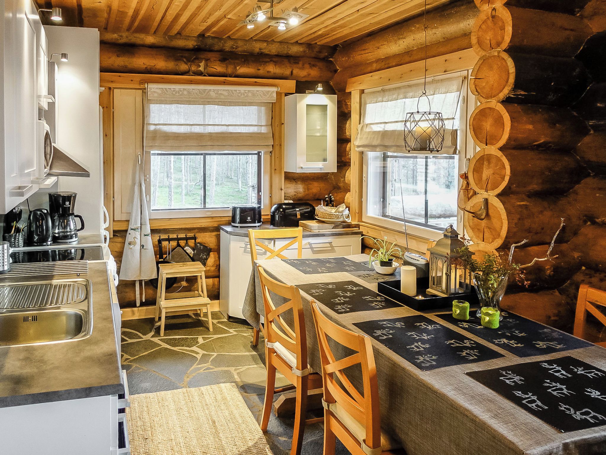 L’intérieur d’une cabane en rondins comprend une cuisine, un coin repas et offre une vue sur la forêt par les fenêtres.