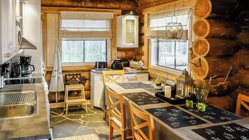 L’intérieur d’une cabane en rondins comprend une cuisine, un coin repas et offre une vue sur la forêt par les fenêtres.