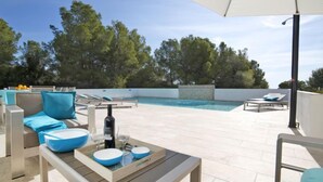 Ein Poolbereich mit Tisch, Liegestühlen und Blick auf Pool und Bäume.