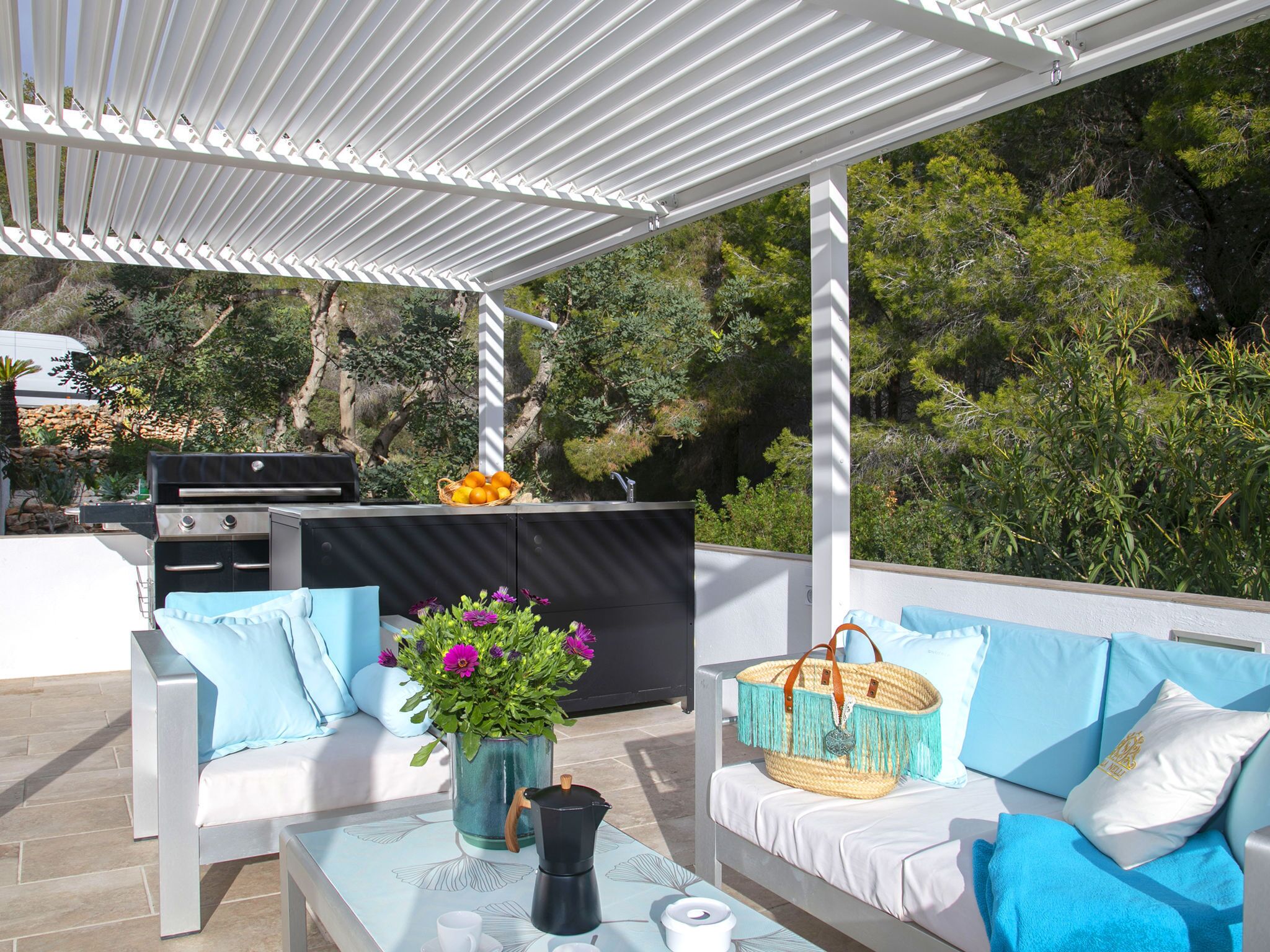 An outdoor patio with white furniture, a grill, and a basket of oranges.