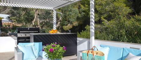 An outdoor patio with white furniture, a grill, and a basket of oranges.