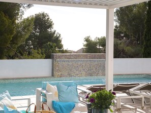 Un espace aménagé au bord de la piscine, avec des chaises longues, un mur carrelé et une vue sur la piscine.